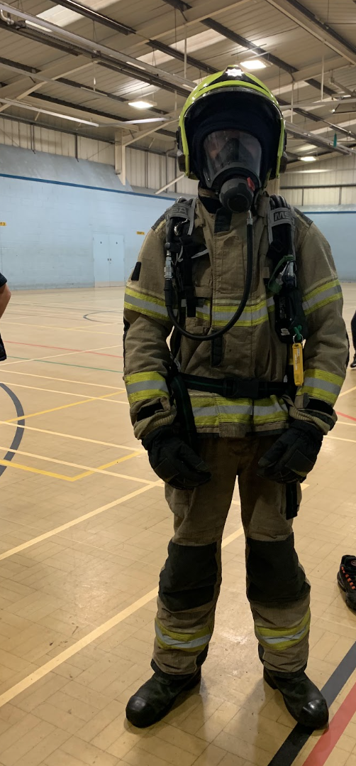 A student in full firefighter kit, helmet, tunic and boots, ready to take part in a drill